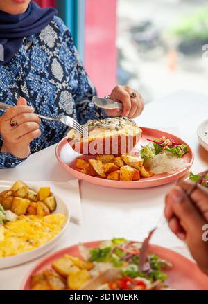 Arabische Frau genießt Brunch-Croissant-Sandwich mit Freunden in einem Restaurant. Stockfoto