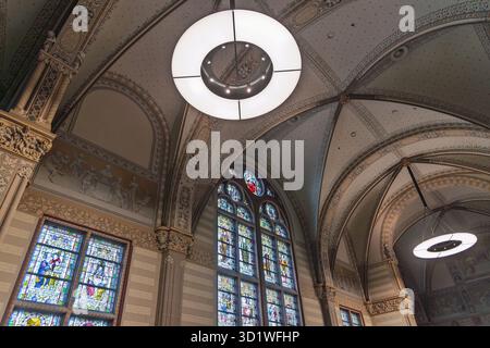 Im historischen Rijksmuseum in Amsterdam mit großen, modernen runden Leuchten verzierte Decke im Stil des Gotischen Neujahrs und Buntglasfenstern. Stockfoto