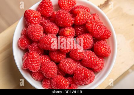 Ansicht von oben nach unten, die den Rahmen füllt, von frischen, leuchtend roten Himbeeren in einer weißen Schüssel Stockfoto