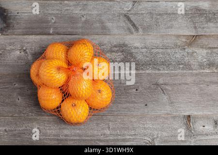 Leuchtend orange Mandarinen in einem orangen Netz auf einer Holzoberfläche. Draufsicht. Stockfoto