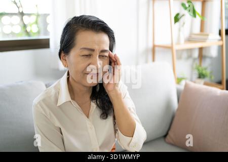 Asiatische Frau mittleren Alters, die die Stirn berührt und Kopfschmerzen hat, die an Migräne oder Depressionen leidet Stockfoto