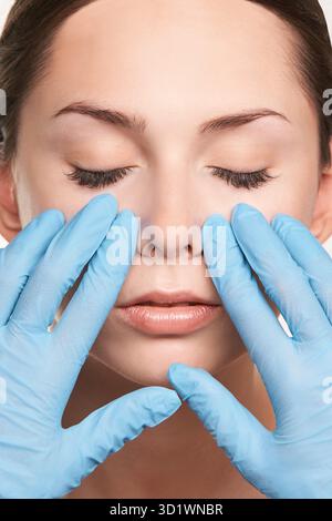 Frau mit geschlossenen Augen erhält Gesichtsmassage von Handschuhen in der Hautpflege Stockfoto