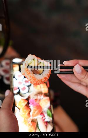 Sushi-Roll mit Avocado und Lachs in Stäbchen Stockfoto