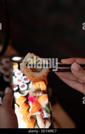 Sushi-Roll mit Avocado und Lachs in Stäbchen Stockfoto