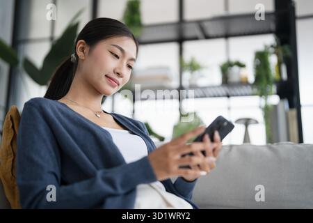Asiatische Frau, die Smartphone-Handy-Süchtige verwendet, die Zeit damit verbringt, soziale Medien auf Sofa zu Hause Handy-Technologie socia zu überprüfen Stockfoto