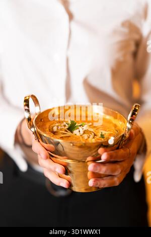 Indisches Curry in Golden Bowl, gehalten vom Kellner Stockfoto
