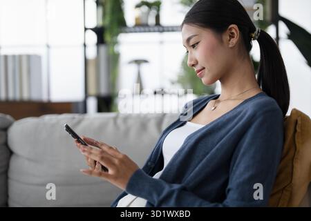 Asiatische Frau, die Smartphone-Handy-Süchtige verwendet, die Zeit damit verbringt, soziale Medien auf Sofa zu Hause Handy-Technologie socia zu überprüfen Stockfoto