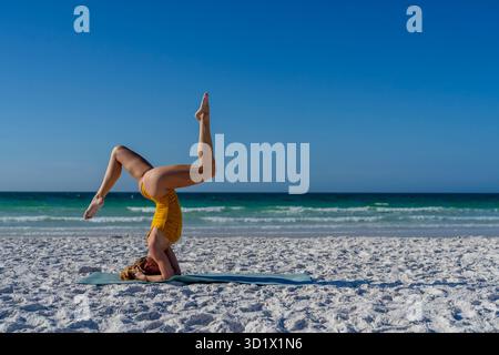 Ein wunderschönes blondes Model übt am frühen Morgen Yoga an Einem weißen Sandstrand Stockfoto