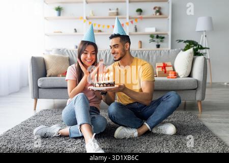 Das Paar feiert den Geburtstag mit Kuchen und Kerzen im gemütlichen Wohnzimmer mit Dekoration Stockfoto