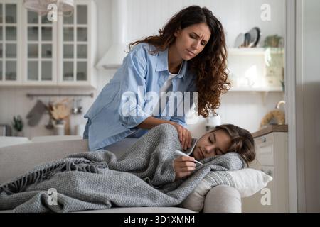Besorgte Elternmutter, die sich um ein krankes Kind kümmert, das zu Hause unter einer Decke liegt und Fieber hat Stockfoto