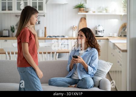 Mutter sitzt auf dem Sofa mit Handy, sieht sich die kranke Tochter an und schreibt dem Arzt Stockfoto