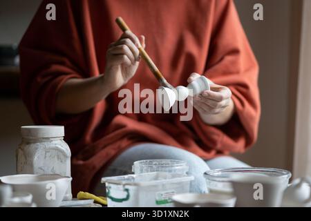 Keramikkeramikerin oder Töpferin, die einen Pinsel hält und Keramikstücke mit Glasur behandelt Stockfoto