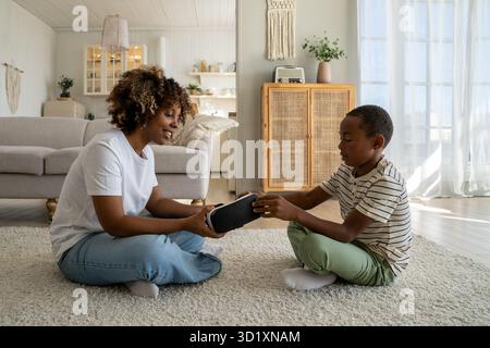 Moderne afroamerikanische Familienmutter und Sohn, die auf dem Boden mit VR-Brille sitzen Stockfoto
