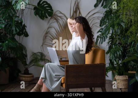 Italienische freiberufliche Mitarbeiterin, die Pause vom Computer nimmt, während sie im Zimmer mit grünen Pflanzen arbeitet Stockfoto