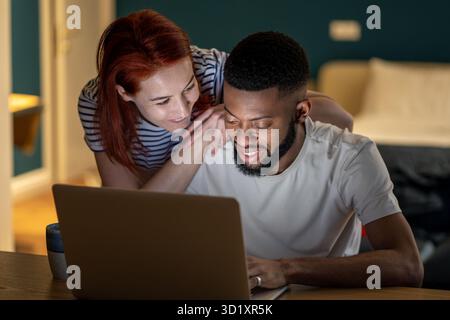 Eine liebevolle junge Frau, die die Aufmerksamkeit eines vielbeschäftigten Ehemanns verlangt, der spät zu Hause an einem Notebook arbeitet Stockfoto