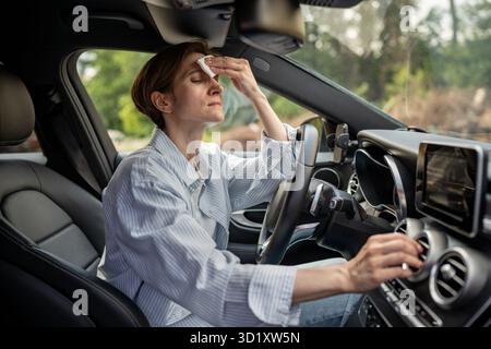Frau fährt Auto mit kaputter Klimaanlage bei heißem Wetter wischt Schweiß auf Gesicht. Stockfoto