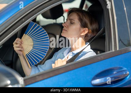 Erschöpfte Frau mittleren Alters fährt Autowellen blauer Fan leidet an Stau im Verkehr. Stockfoto