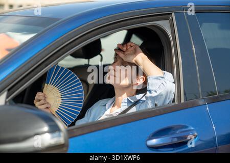 Erschöpfte Frau mittleren Alters fährt Autowellen blauer Fan leidet an Stau im Verkehr. Stockfoto