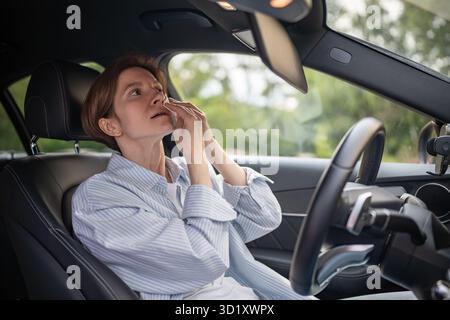 Frau fährt Auto mit defekter Klimaanlage bei heißem Sommerwetter, wischt Schweiß-Papierserviette ab. Stockfoto