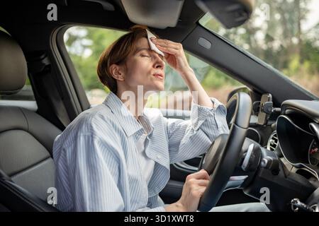 Frau fährt Auto mit kaputter Klimaanlage bei heißem Sommerwetter. Zum Wischen von Schweißpapierservietten. Stockfoto