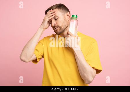 Ein müder Mann leidet an Hitze und Blutdruck, legt eine Flasche kaltes Wasser an den Hals, fühlt sich dehydriert. Stockfoto