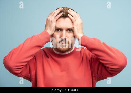Verwirrter, bärtiger Mann, der den Kopf in die Kamera schaut, auf blauem Hintergrund. Stockfoto