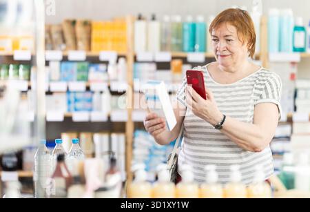 Ältere Frau in der Apotheke scannt QR-Code auf Creme Stockfoto