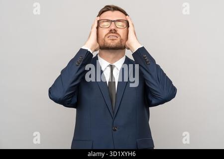 Erschöpfter depressiver Geschäftsmann in Brille mit geschlossenen Augen, der sich schlecht isolierter Hintergrund anfühlt. Stockfoto