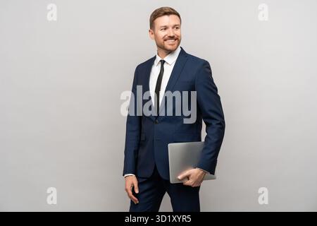 Erfolgreicher männlicher Geschäftsmann selbstbewusster Look mit Laptop in der Hand stehend isolierter grauer Hintergrund. Stockfoto