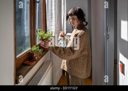 Ein Mädchen, das mit Wasser spritzt, Topfblumen tränkt, und es genießt, Pflanzen anzubauen Stockfoto