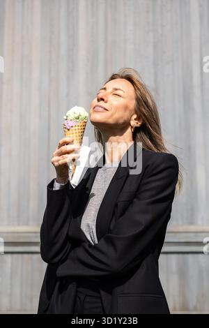 Lächelnde Frau genießt Eis in Kegel, fröhlich baden in Sonnenstrahlen im Sommer. Stockfoto
