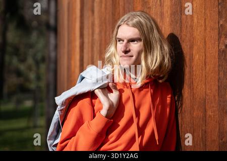 Glücklicher europäischer blonder Kerl lächelt, blickt in die Ferne und entspannt draußen genießt sonniges Wetter. Stockfoto