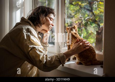 Frau streichelt Katze, die zu Hause auf der Fensterbank sitzt und Kommunikation genießt. Katzenliebhaber. Stockfoto