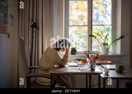 Gestresste Frau mit Burnout sitzt am Tisch und hält den Kopf mit Händen, die sich schlecht fühlen, Arbeitsproblem haben Stockfoto