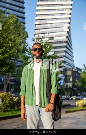 Selbstbewusster afroamerikanischer Mann in Sonnenbrille fokussierte Blicke im Wolkenkratzer-Hintergrund der Stadt. Stockfoto