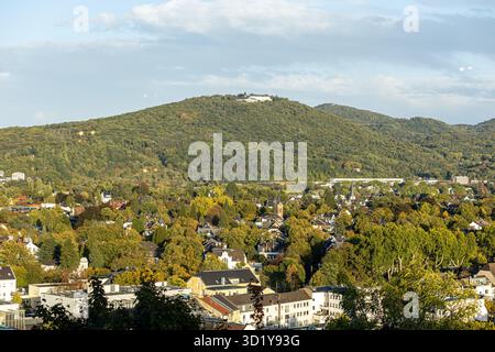 Ein atemberaubender Blick fängt eine malerische Stadt ein, eingebettet zwischen grünen Hügeln im Herbst. Buntes Laub unterstreicht die ruhige Landschaft unter einem klaren Himmel Stockfoto
