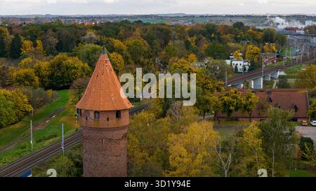 Herbstblick aus der Luft in der Nähe von Malbork, Polen. Ein roter Backsteinturm mit orangefarbenem Dach erhebt sich an Bahngleisen und roten Ziegelgebäuden. Weiches, bedecktes Licht und Di Stockfoto