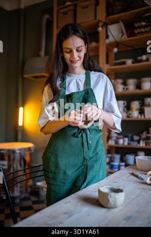 Lächelnde Handwerkerin formt Tonschalen in der Töpferwerkstatt, Klasse. Keramiklehrer und Kleinunternehmen Stockfoto