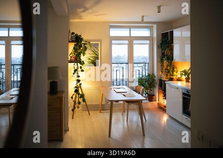 Einladende Einrichtung des Apartments mit sanftem Lampenlicht im Spiegel, warm leuchtender Küche und Flur Stockfoto