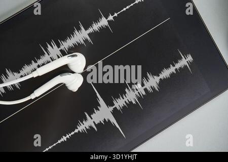 Podcast-Aufzeichnung. Ohrstöpsel und Soundtrack am Tablet. Graues Schwarzweiß. Hörbuch und Podcasting. Audiotechnologie. Teekanne für die Heimschule Stockfoto