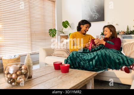 Paare tauschen Geschenkbox auf Sofa im Wohnzimmer mit Kerzenständern und Ornamenten aus Stockfoto