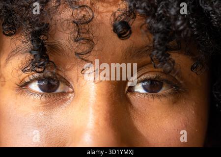 Face filling frame focusing eyes eyebrows revealing warm brown skin pores while framing curly hair Stockfoto