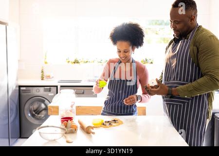 Diverse Paare in Schürzen schneiden Keksteig mit Nudelnadel und Keksschneider auf Kücheninsel Stockfoto