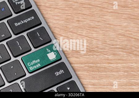 Computertastatur mit Kaffeepause-Taste auf hölzernem Hintergrund. Tastatur mit grüner Taste Kaffeepause-Symbol. Kopierbereich. Stockfoto