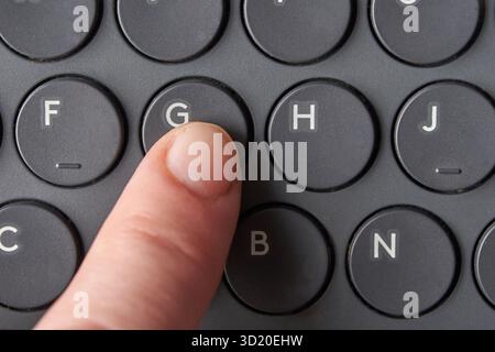 Nahaufnahme des Fingerdrucks der Taste g auf der runden schwarzen Tastatur Stockfoto