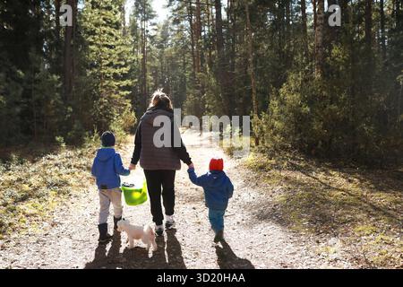 Kinder und Erwachsene gehen Hand in Hand mit einem kleinen Hund auf einem sonnigen Waldweg im Frühjahr Stockfoto