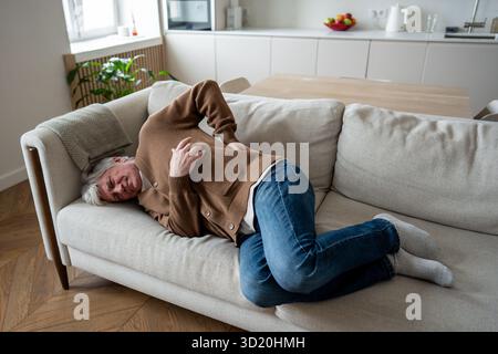 Exazerbation der Hernie. Der kämpfende alte Mann, der sich in Rückenschmerzen auf der Couch zusammengerollt hat, leidet an Osteochondrose Stockfoto
