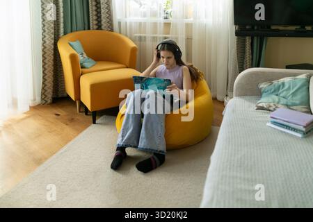 Die junge Frau genießt es, sich mit einem Buch zu entspannen, während sie in einem gemütlichen Sitzsack-Stuhl in einem hellen Wohnzimmer sitzt Stockfoto