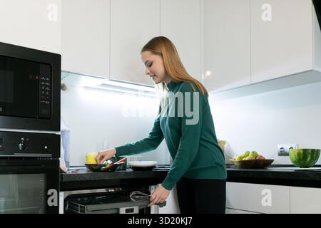 Junge Frau, die in einer modernen Küche mit frischen Zutaten und Geräten eine Mahlzeit zubereitete Stockfoto