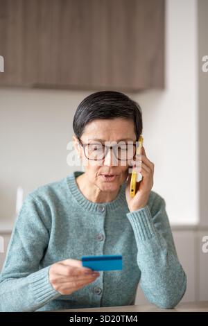 Naive reife Frau liest während eines verdächtigen Smartphone-Anrufs die Kreditkartennummer laut vor Stockfoto